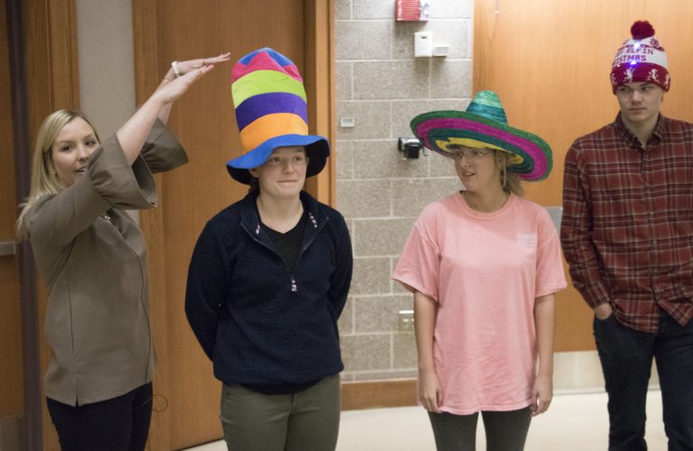 four people standing, two wearing hats