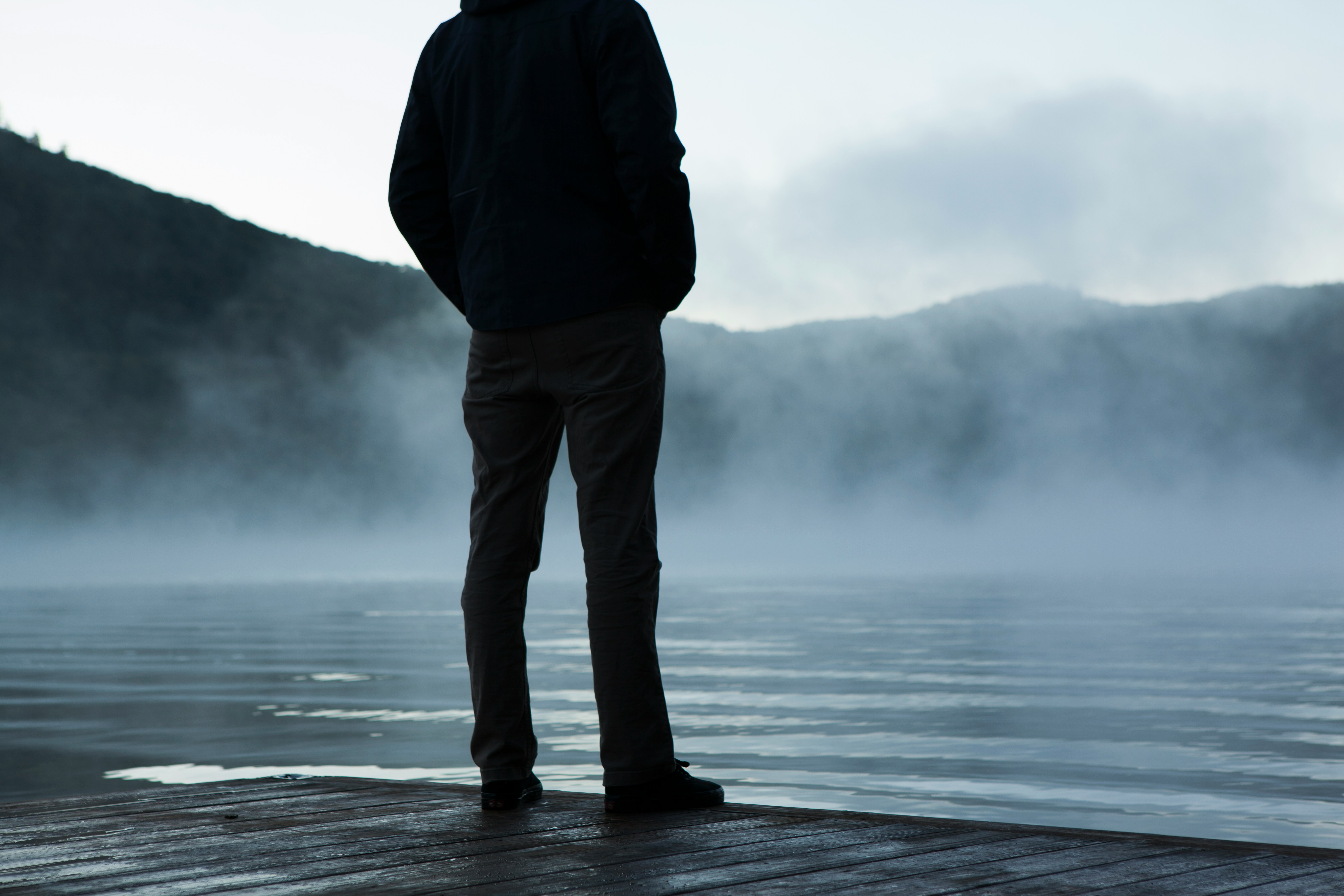 A man standing on dock by foggy lake