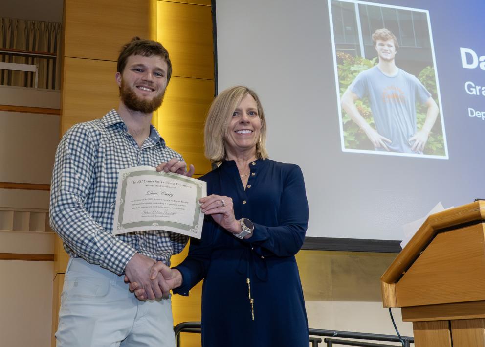 Two people on a stage shaking hands and holding a certificate