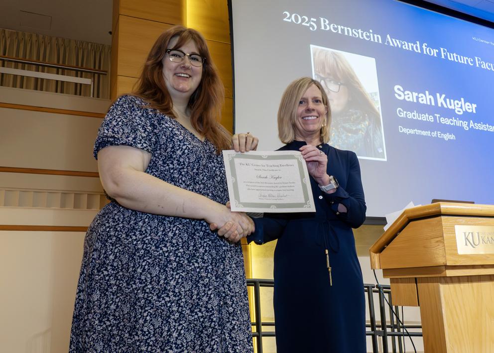 Two people on a stage shaking hands and holding a certificate