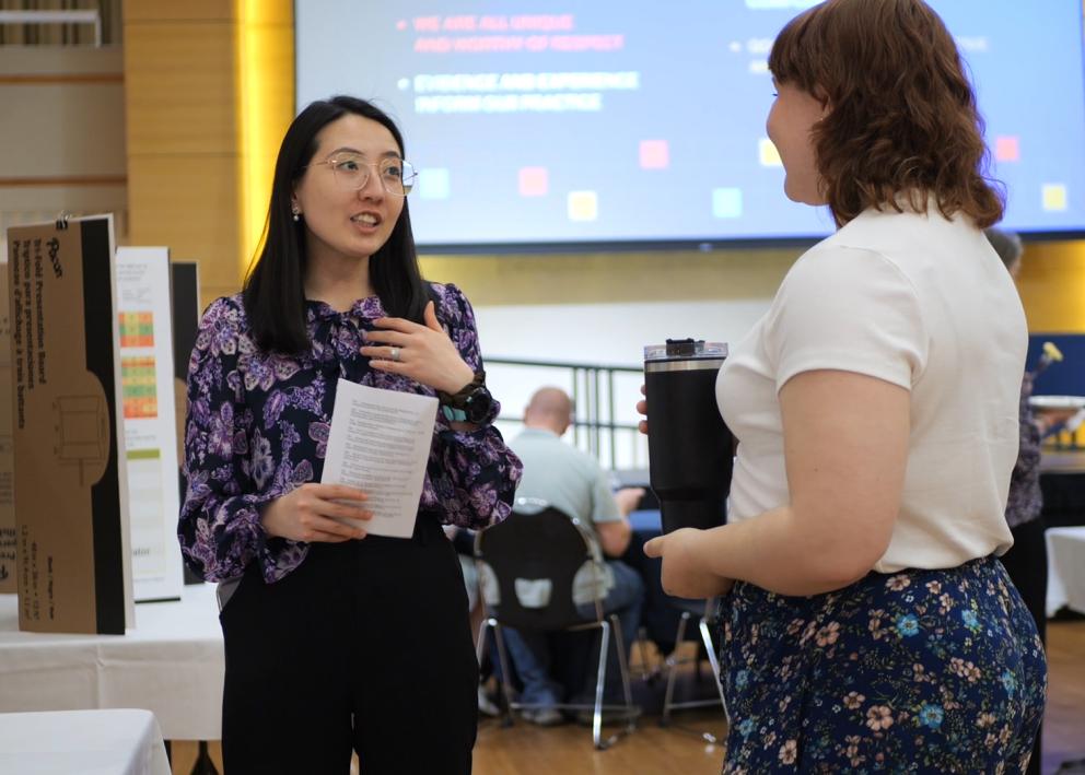 Poster presenter speaks with visitor with academic poster