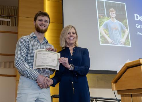 Two people on a stage shaking hands and holding a certificate
