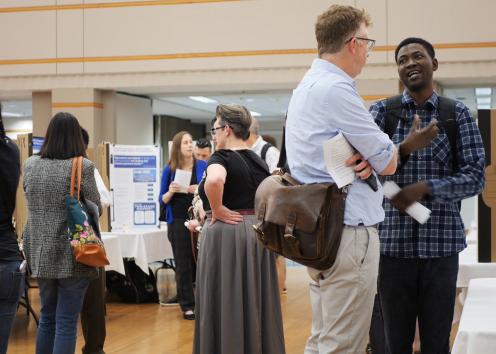 Poster presenter speaks with visitor with academic poster